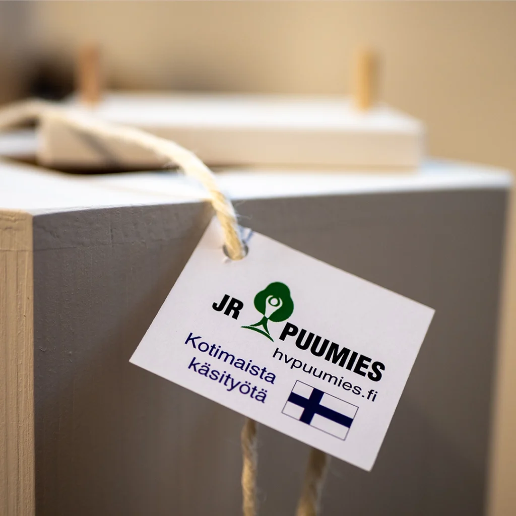 Lähikuva puisesta uurnasta, jossa on lappu, jossa lukee kotimaista käsityötä